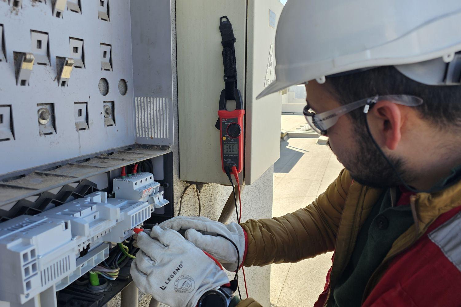 Técnico midiendo parámetros con pinza amperimétrica en el tablero de un inversor, en la cubierta de un edificio