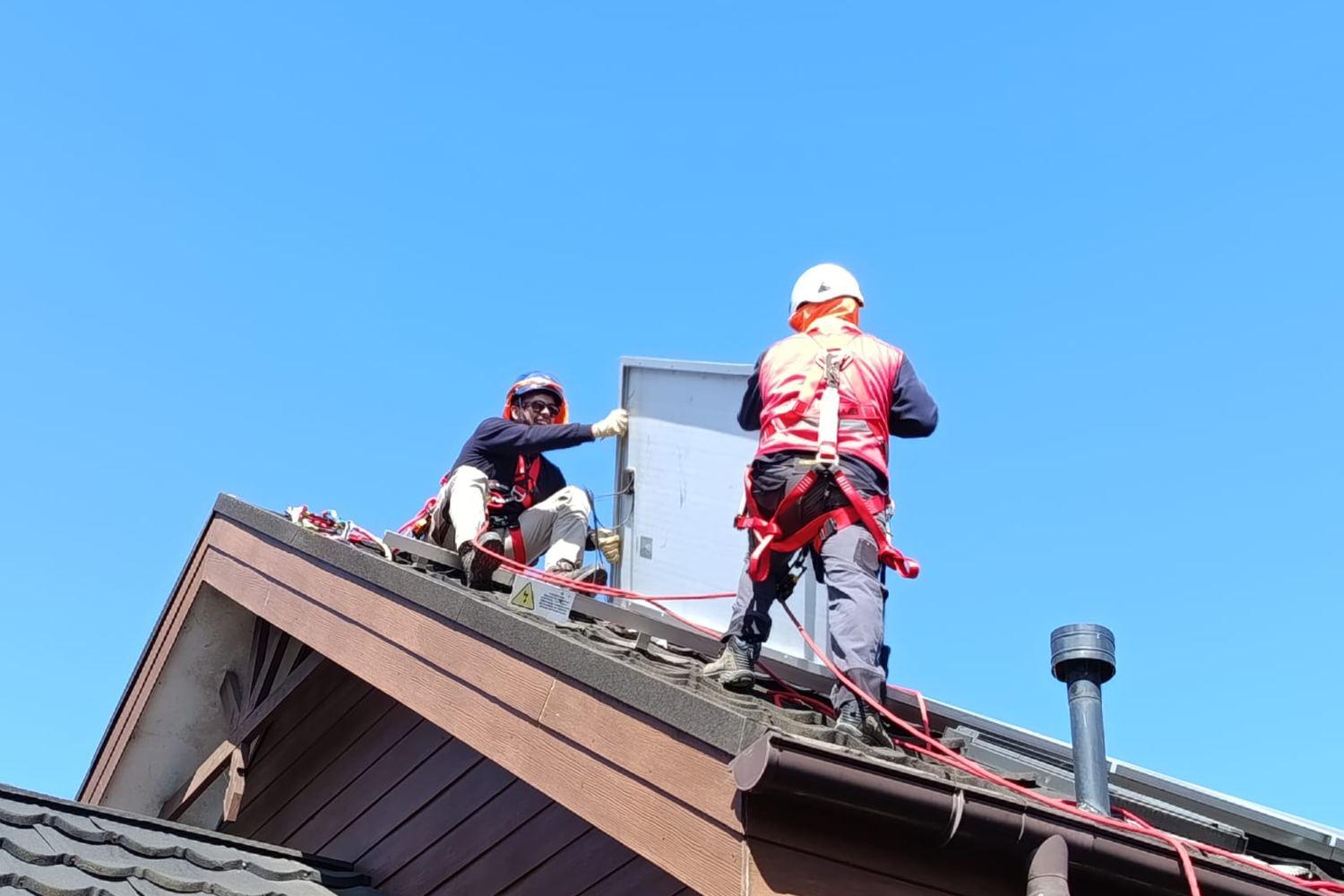 Dos operarios con arnés y casco instalando un panel en la cumbrera de un techo